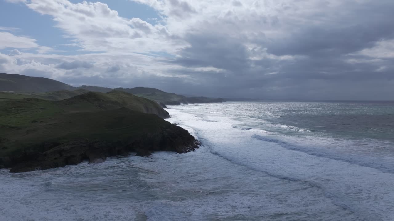 Aerial drone view of Cantabrian coastal villages surrounded by lush green meadows ending in gentle cliffs over the turquoise sea, capturing the harmony between nature and rural life under a bright sky