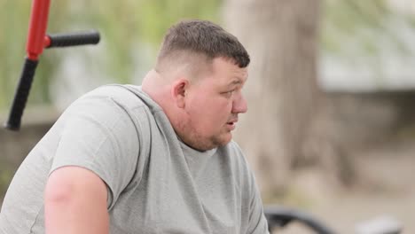 a tired fat man rests takes a breather during training overweight man on outdoor exercise machine a tired fat man rests takes a breather during training overweight man on an outdoor exercise machine dyspnea the man is losing weight
