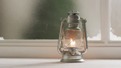 Video-of-glowing-vintage-oil-lamp-over-frozen-and-snowy-window