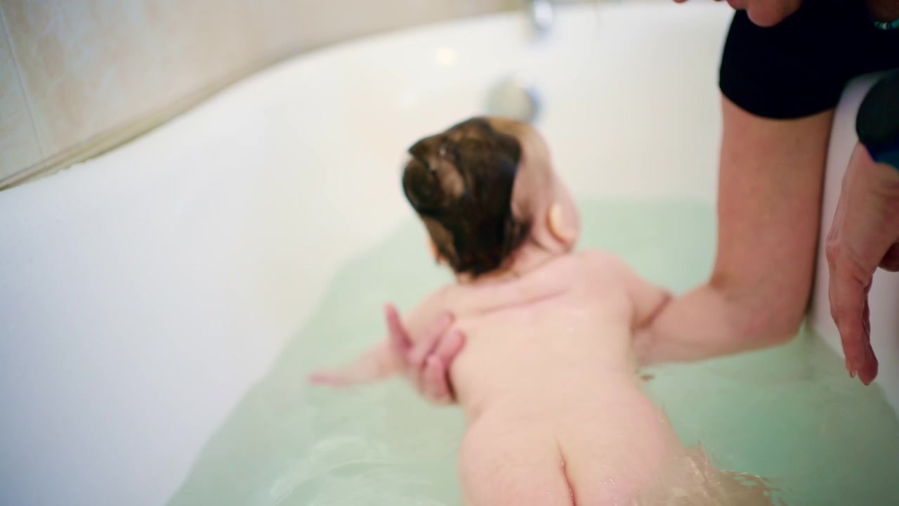 Close up of newborn baby being gently bathed by caregiver during bath time