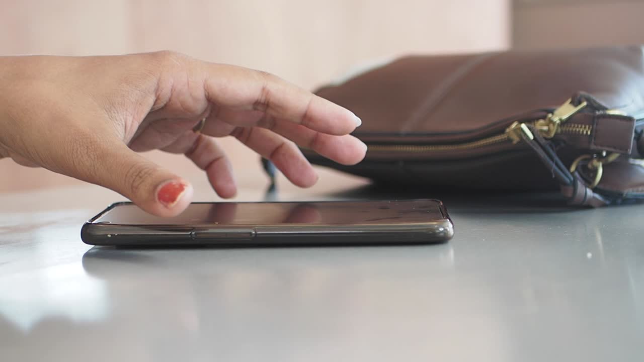 Woman holding phone next to a bag on a table