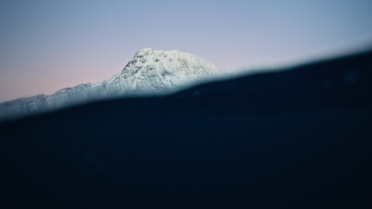 Low waterline Arctic Ocean waves with bright snow covered Norway mountains