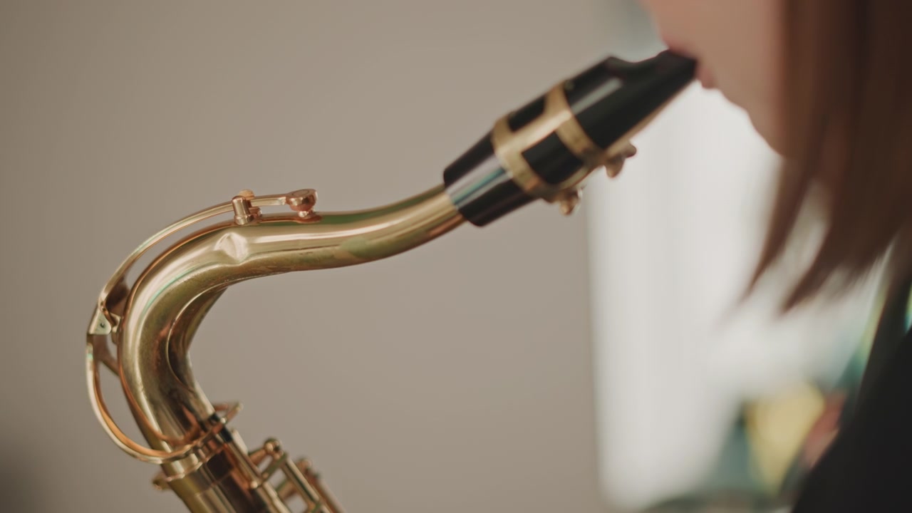 Élève de l'orchestre testant le son du saxophone en répétition, gros plan sur le corps et l'embouchure, vérifications minutieuses du souffle et de l'intonation, ambiance de répétition d'ensemble scolaire avec une préparation concentrée.