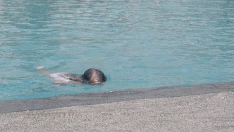 Chica-Feliz-Se-Aferra-Al-Borde-De-La-Piscina-Del-Hotel-En-Cámara-Lenta