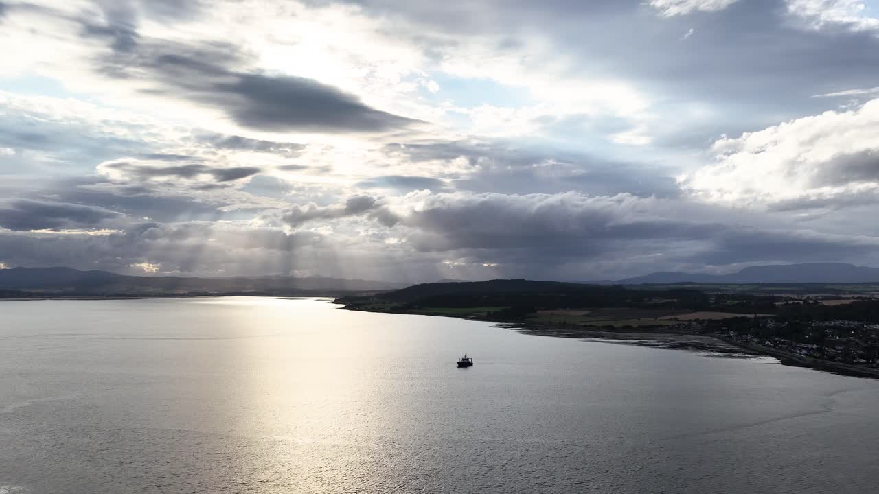 A lone boat drifts on calm water beneath dramatic sunset clouds, wide aerial view