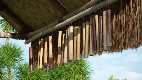 bamboo wind chimes hang from thatched roof of outdoor shed with wooden poles