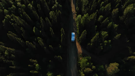 aerial view following camper van driving on a forest dirt road, summer in lapland