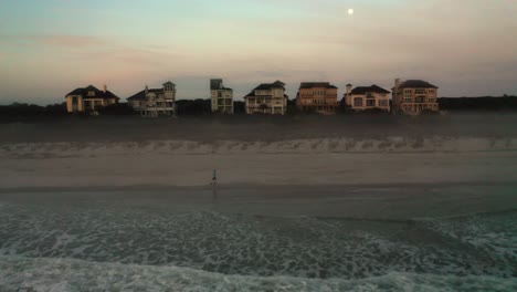 aerial, man running alone on the beach early morning, luxurious houses for the wealthy in background