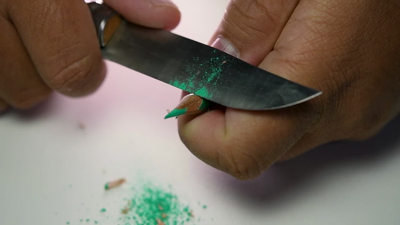 날카로운 칼로 연필과 색연필을 천천히 갈고 있는 손의 영상