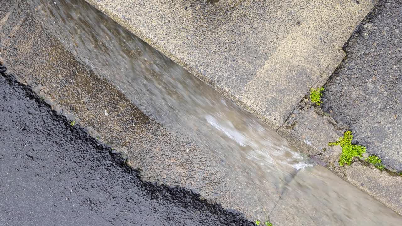 은 비가 오는 날씨에 도로 의 쪽 배수구에서 빠르게 흐르는 물이 흐르고 있습니다.