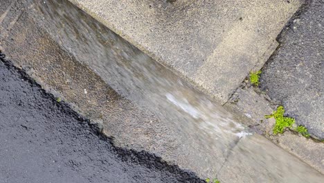 agua de lluvia de flujo rápido que fluye por el drenaje lateral de la acera en la carretera durante el clima lluvioso húmedo