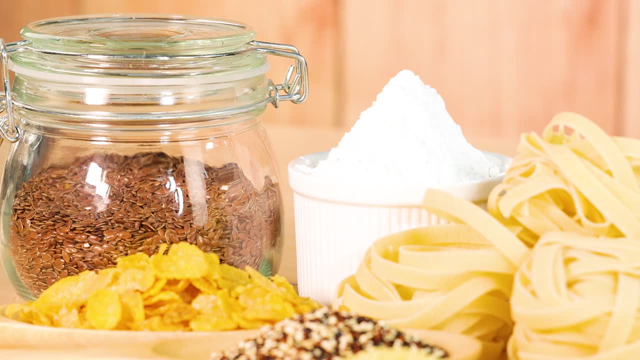 A variety of grains and pasta arranged on a wooden surface with natural lighting, showcasing diverse textures and colors