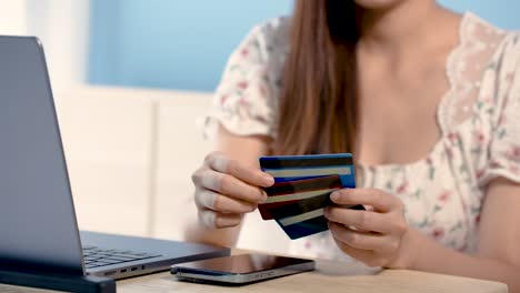 4k 50fps, mujer asiática mano de primer plano titular de tarjeta de crédito tres en la mano, sentado frente a una computadora portátil, eligiendo una tarjeta de crédito. para preparar compras en línea, sentado en la cama, concepto de compras en línea