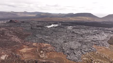 iceland's barren landscape reveals rugged volcanic terrain with steam rising from geothermal activity under a cloudy sky