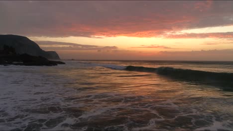 flying backwards close over the watersurface while waves building up and breaking with beutigul rocks szenerie at praia do castelejo in sagres portugal while red orange sunset sunrise