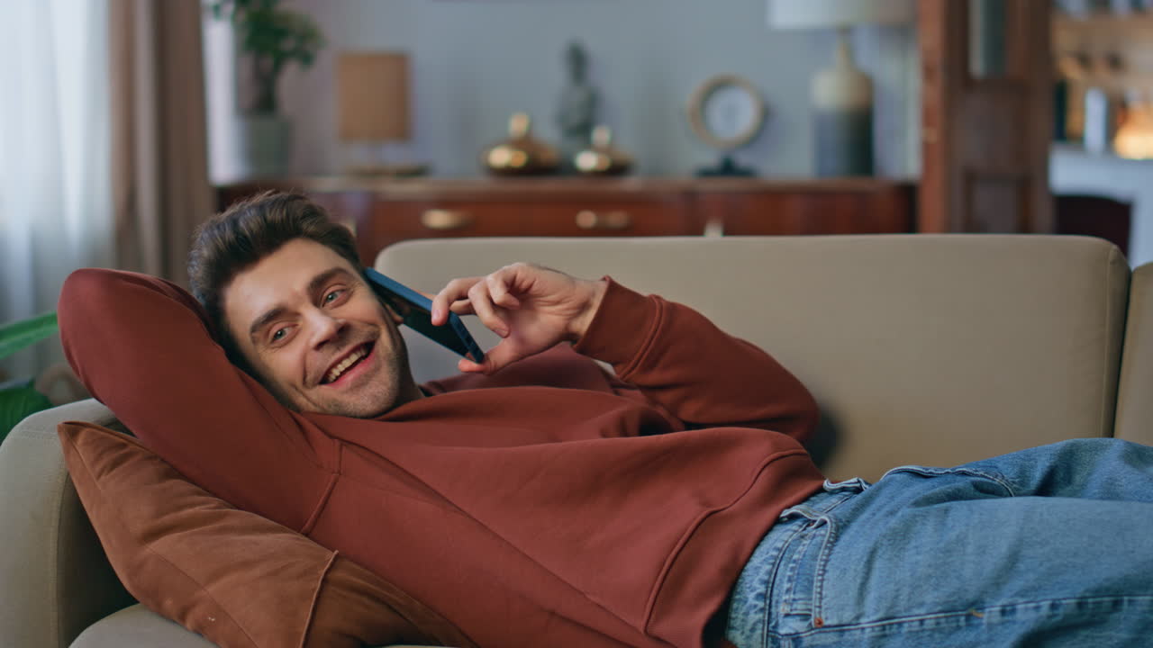 Happy student talking cellphone lying couch close up. Positive man enjoy call