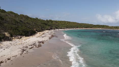 Waves gently wash over the shore at Half Moon Bay Beach Antigua on a bright sunny day