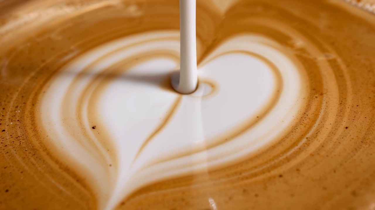 Lattiera che versa latte montato a vapore, creando una latte art a forma di cuore in una tazza al bar, con anelli di crema.