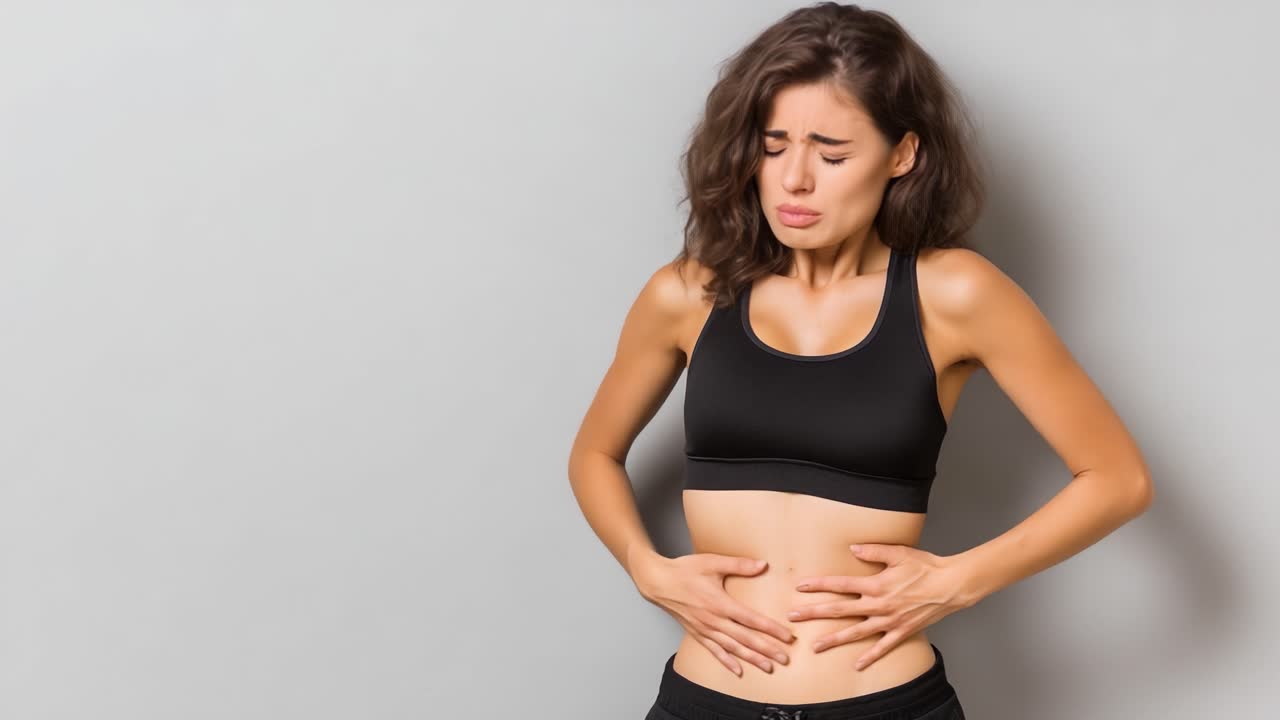 Una giovane donna alle prese con un disagio addominale, che esprime dolore e sofferenza mentre si tiene lo stomaco in un ambiente minimalista su uno sfondo neutro