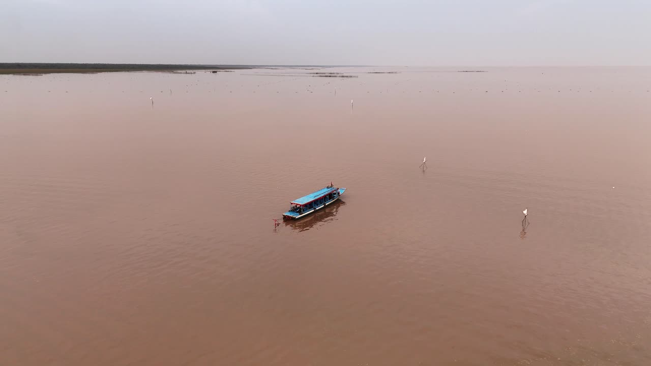 4K Drone descends toward a floating Cambodian blue boat on Tonle Sap, while the distant shoreline stretches across the horizon.
