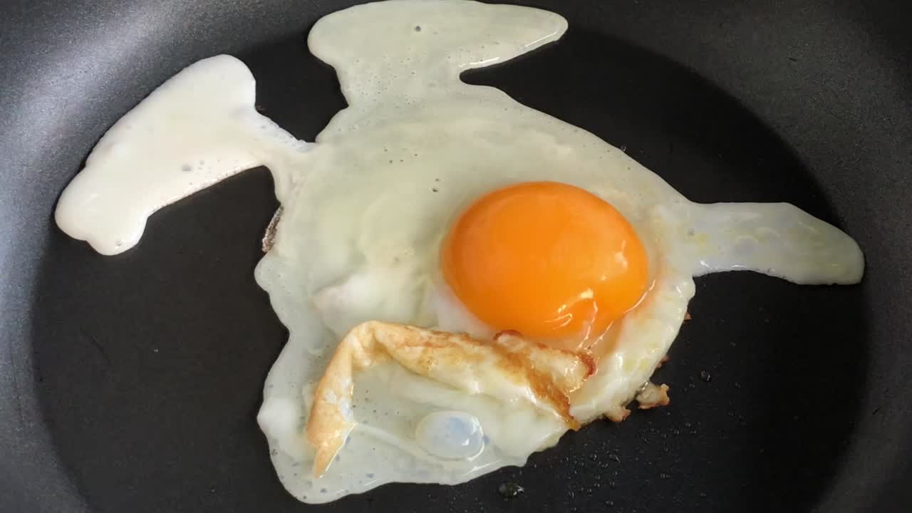 Telur goreng di wajan. Telur pecah jatuh ke wajan penggorengan. Dengan latar belakang bising dan bokeh buram