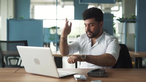 portrait-of-a-handsome,-stylish-young-man-of-Arab-descent-sitting-in-a-modern-business-center-office-with-a-laptop,-working-furiously,-upset-by-failure,-closing-the-laptop