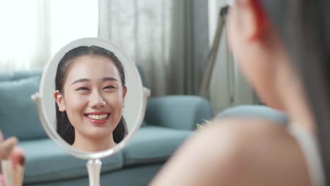 집에서 메이크업을 한 후 미소 짓는 아름다운 젊은 아시아 여성의 거울 반사