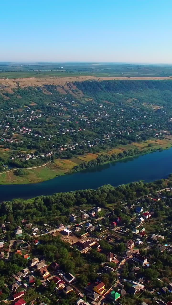 Picturesque city with narrow river dividing it into two banks. Urban landscape at sunny daytime from top. Hazy horizon at backdrop. Vertical video
