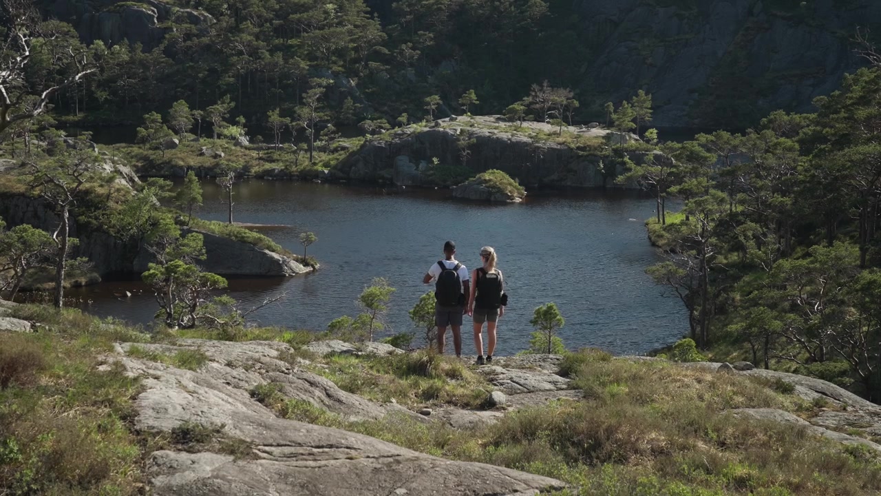 Escursionisti camminano lungo un piccolo lago di montagna in Norvegia, si fermano sulla riva per godersi il paesaggio, poi continuano la loro escursione attraverso un tranquillo paesaggio alpino.