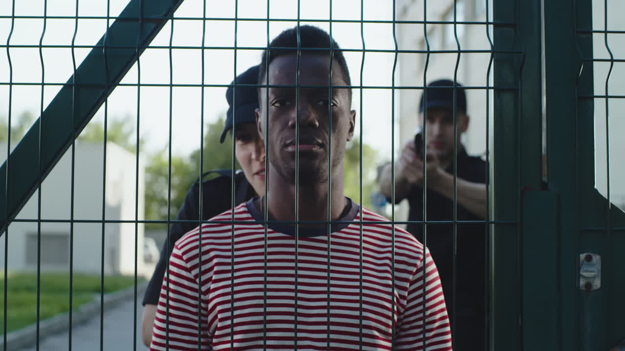 police Officers Arresting Black Guy Near Grid Zoom out View of Woman in Police Uniform Fastening Handcuffs on Indifferent African American Man Near Grate during Arrest on City Street