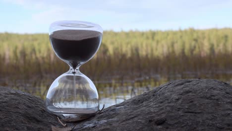 weiße männliche hand mit grünem wollrock rotierendes sanduhr auf dem felsen