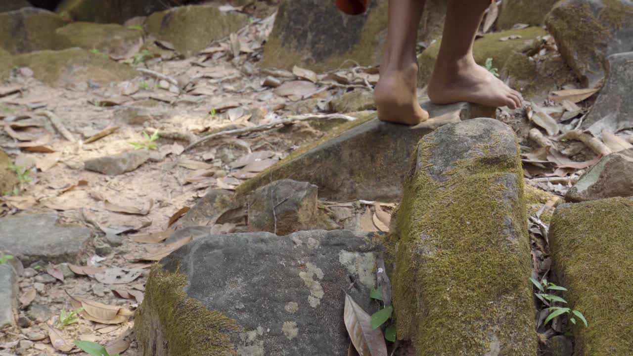 Bare footed Monk in saffron robes walking over Angkorian sandstone rocks