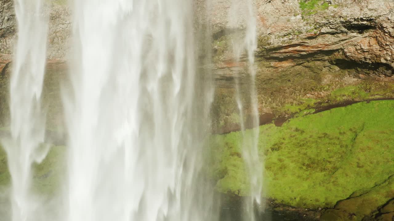 Guy running through cave behind Seljalandsfoss waterfall in Iceland