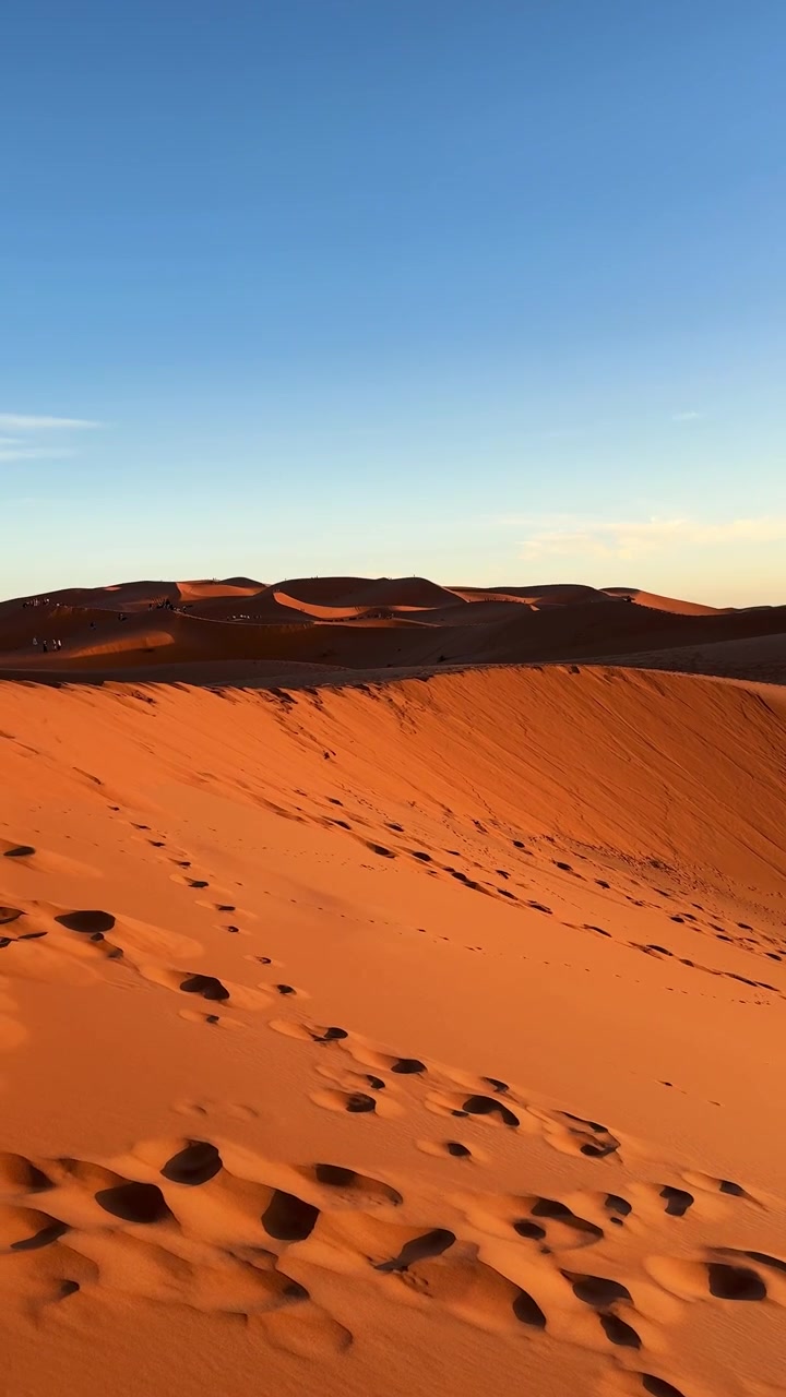 Vertical social media video sweeping across golden Erg Chebbi sand dunes with footprints and dramatic desert ridgelines during sunset in Morocco