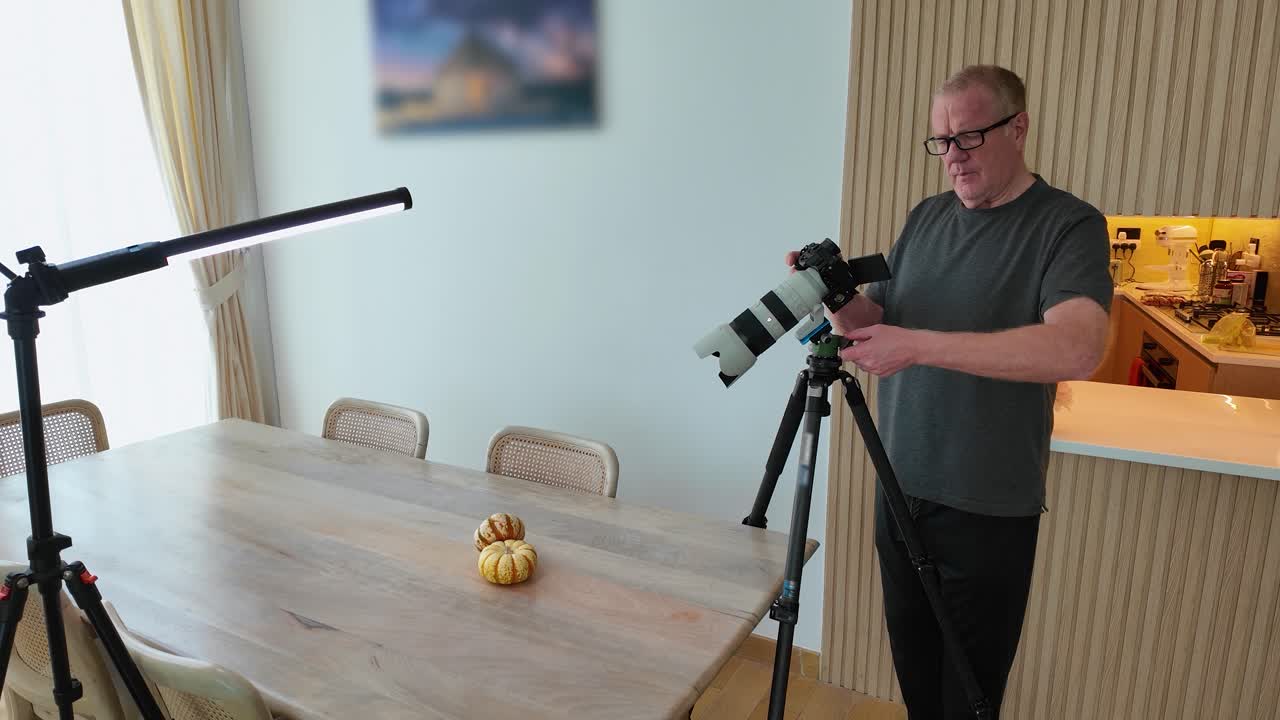 Older man doing macro photography with a professional camera and lens of small, decorative pumpkins on his dining room table with cheap tube and natural lighting