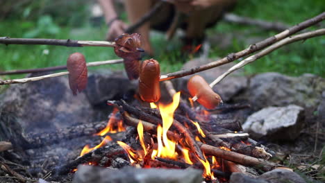 group of friends grilling sausages on a small bonfire at the forest - a perfect activity for summer adventure - close up shot