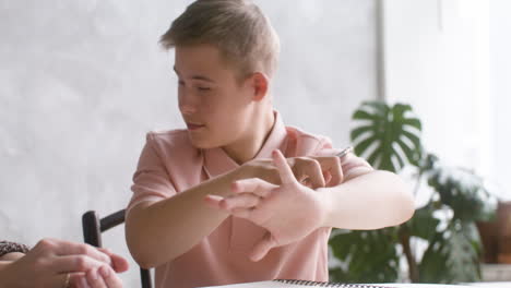 close-up view of a boy with down syndrome doing homeworks sitting at table in the living room at home. he is talking with his mother