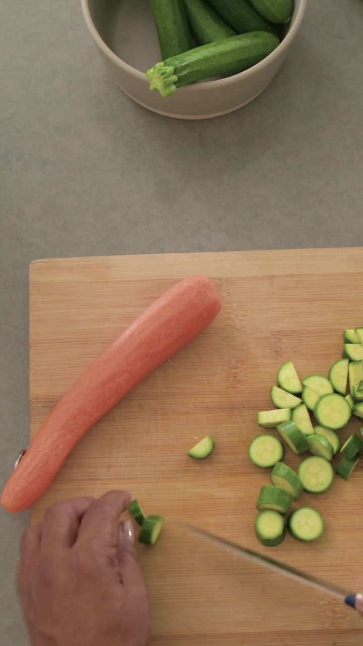 Video verticale: Raccogliendo zucchine, un cuoco le affetta per cena su un tagliere con un coltello a casa, con un top rosa.