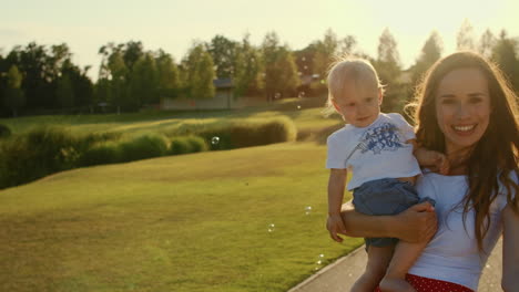 woman holding boy on hands. toddler with mother playing with soap bubbles