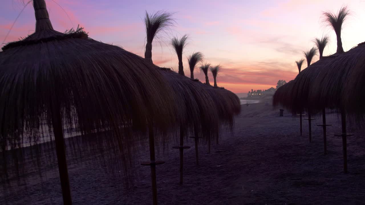 4k imágenes de puesta de sol gimbal playa tropical con paraguas tiki en marbella, málaga, españa, costa del sol, destino de ensueño de vacaciones