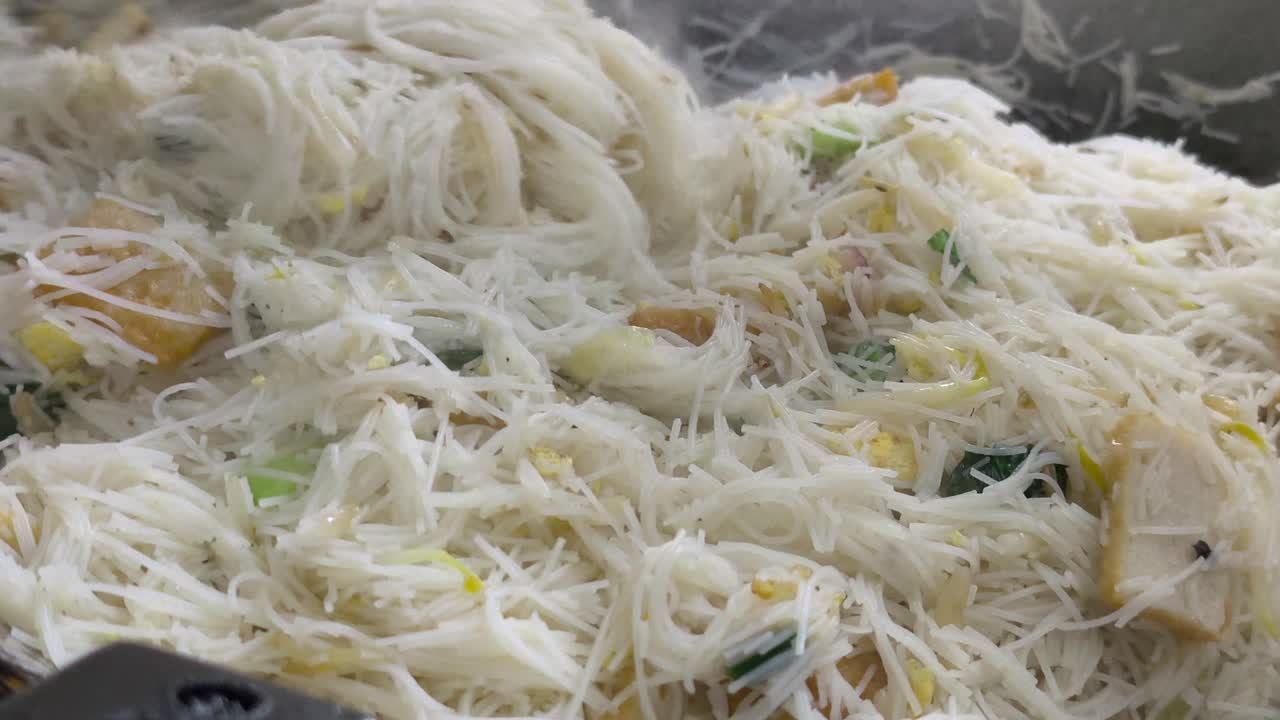 Chef is frying bihun (rice vermicelli) mixed with vegetables, egg, and spices. This flavourful dish is a popular Malaysian food, often served as a quick meal