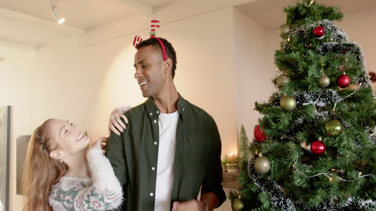 Laughing couple decorating Christmas tree at home, enjoying festive holiday spirit, copy space