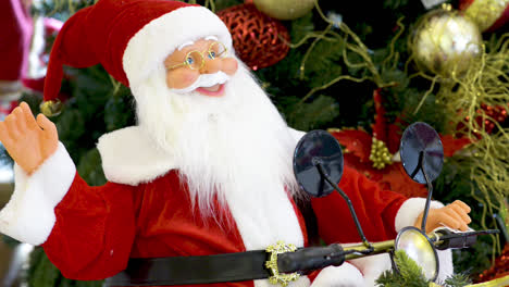 poupée du père noël agitant et faisant de la moto devant l'arbre de noël