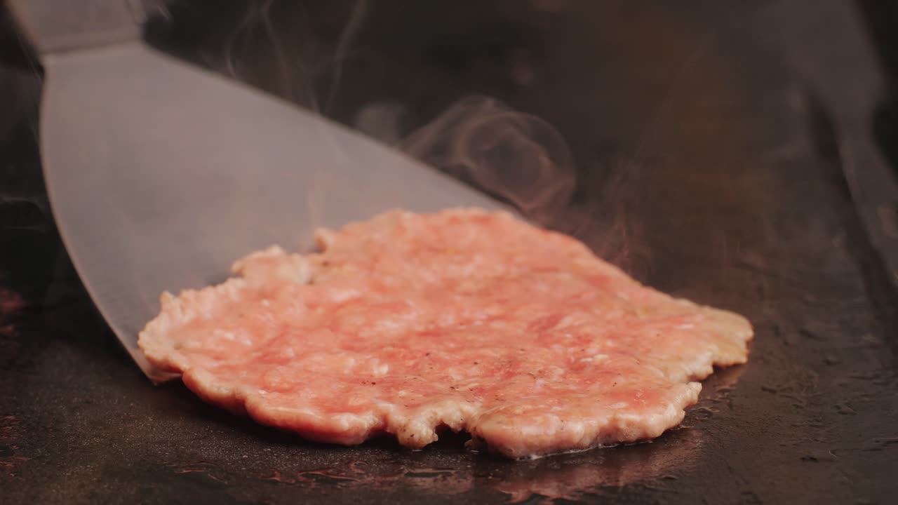 Cooking American fat smash burger on grill close-up. Beef or pork cutlet smashing by burger press. The chef in kitchen of the restaurant making cutlets for burgers - smash burger beefsteak. Fast and street food concept. High quality 4k footage