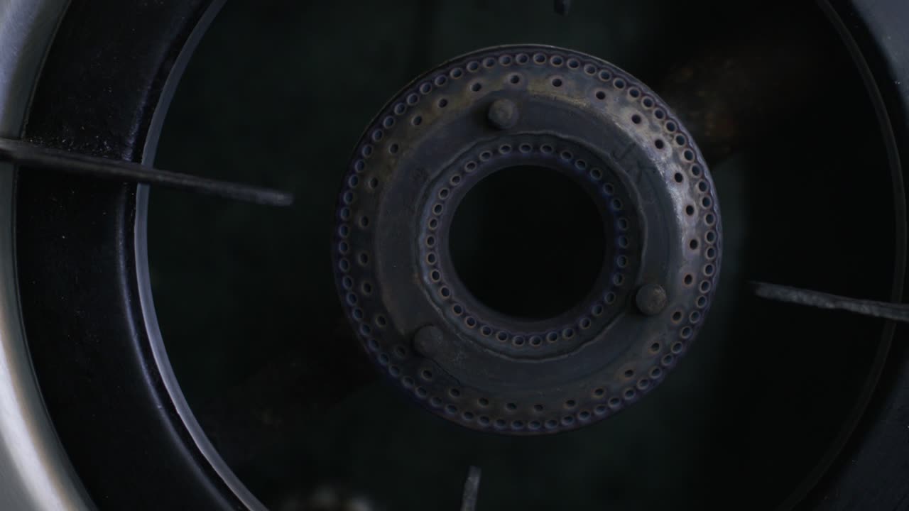 A closeup top view of a stovetop and a person out of the frame igniting it