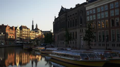 An-early-morning-scene-in-Amsterdam,-Netherlands-with-city-life-reflected-in-perfectly-calm-water-in-a-canal