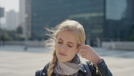 portrait beautiful blonde woman commuter looking serious running hand through hair in windy city sunny urban day slow motion