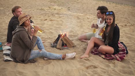 grupo de jóvenes brindando con botellas de cerveza y teniendo una fiesta en la playa en un día de verano diciendo saludos con cerveza en 4k