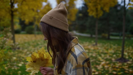 side portrait of smiling attractive girl walking with yellow leaves in hands.