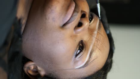 beautician wearing black gloves is using a rotary tattoo machine for applying permanent makeup on a customer's eyebrows